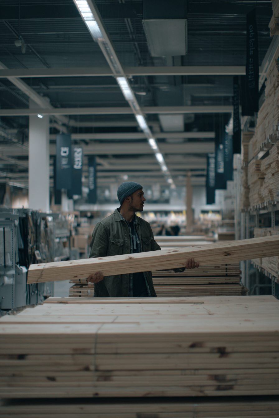 A pine board in a home improvement store being checked for straightness by sighting along its edge under bright indoor lighting
